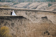 A stylish bridegroom in a black suit kisses a beautiful bride's hand in a lace dress against the background of gray rocks and hills. Autumn wedding portrait of loving newlyweds. Film effect.