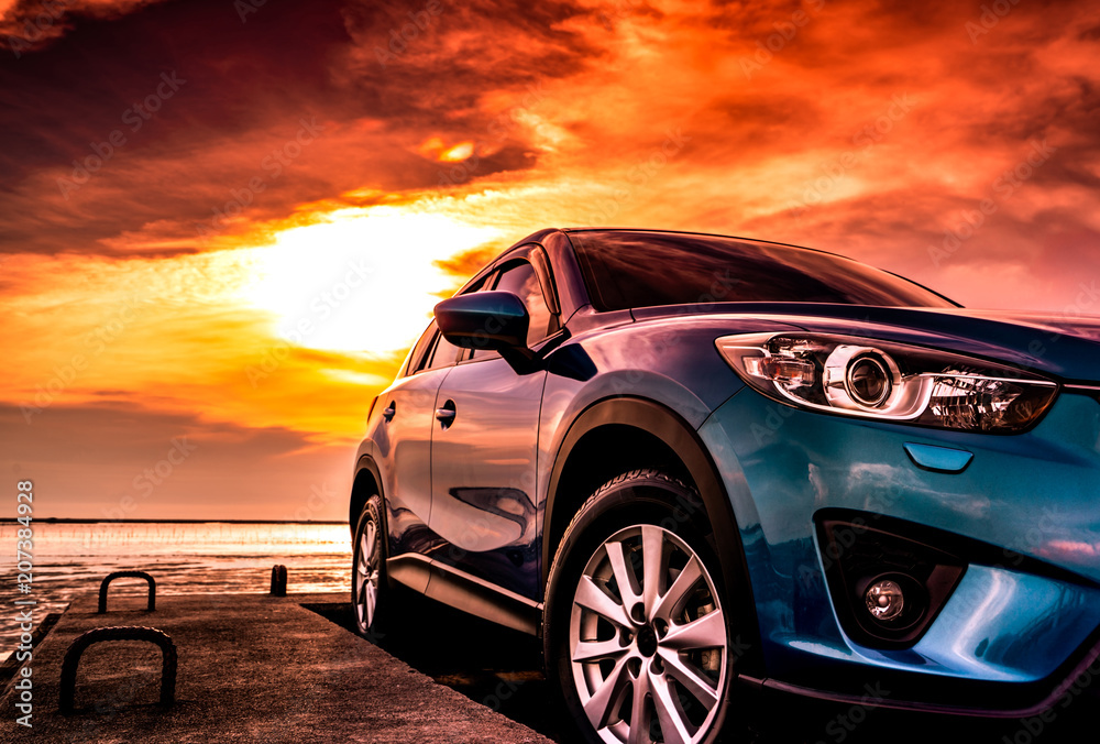 Blue compact SUV car with sport, modern, and luxury design parked on concrete road by the sea at sunset. Front view of beautiful hybrid car. Driving with confidence. Travel on vacation at the beach. - obrazy, fototapety, plakaty 