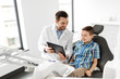 © Syda Productions - medicine, dentistry and healthcare concept - smiling male dentist showing tablet pc computer to kid patient at dental clinic
