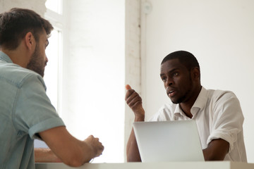 Wall Mural - Serious African American worker talking to Caucasian colleague, discussing work issues, negotiating about shared business project during corporate company meeting in office. Multiethnic collaboration