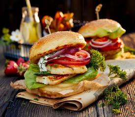 Wall Mural - Vegetarian burger with grilled halloumi cheese, fresh lettuce, tomato, cucumber and onion with the addition of yoghurt mint sauce on a wooden rustic table