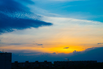Wall Mural - atmospheric blue cloudy sky behind silhouettes of city buildings. cobalt and orange background of su