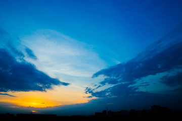 Wall Mural - atmospheric blue cloudy sky behind silhouettes of city buildings. cobalt and orange background of su