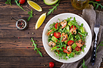 Wall Mural - Fresh salad bowl with shrimp, tomato, avocado and arugula on wooden background close up. Healthy food. Clean eating. Top view. Flat lay.