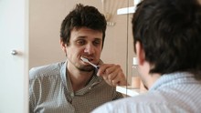 Tired Man Who Has Just Woken Up Brush His Teeth, Looks At His Reflection In The Mirror And Sees His Scruffy Appearance.