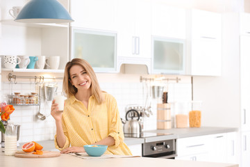 Wall Mural - Beautiful young woman having breakfast and drinking milk in kitchen