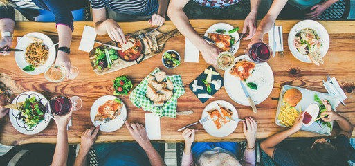 Family or friends summer party or outdoor dinner. Flat-lay of group of people at big table in cafe eating verious food together. Summer gathering or celebration concept