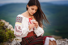 Attractive Woman In Traditional Romanian Costume On Mountain Green Blurred Background.