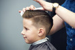 Barber shop. Hairdresser makes hairstyle to a boy using styling gel.