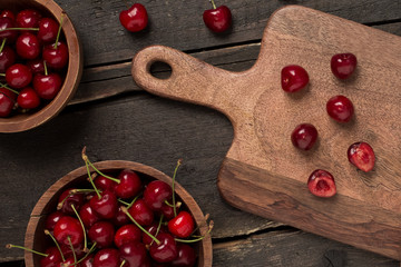 Fresh cherries close up on a wooden board with two plates on a wooden table