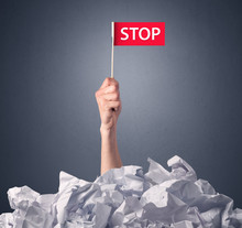 Female Hand Emerging From Crumpled Paper Pile Holding A Red Flag With Stop Written On It 
