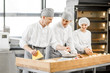 © rh2010 - Three young bakers in uniform forming dough for baking on the wooden table standing together at the modern manufacturing