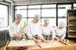 © rh2010 - Group of young workers in uniform filling buns for baking on the wooden table standing together at the modern manufacturing
