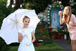 Śliczna dziewczynka w białej sukience trzyma biały parasol, w pierwszy dzień komuni.