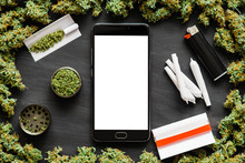 Black Smartphone With A White Screen Mock Up Weed, Grinder, Lighter, Joint A Lot Of Marijuana, Fresh Buds Of Cannabis Many Weed. Copy Spase Copy-space Top View