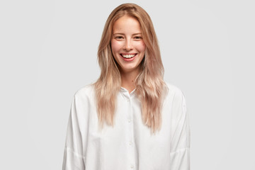 Wall Mural - Cheerful beautiful European female with pleasant smile, has white perfect teeth, wears oversized shirt, has straight hair, laughs on funny joke. People, positive emotions and feelings concept