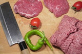 Fototapeta  - Sirloin steaks, minced beef, red cherry tomatoes and green pepper with Japanese knife on wooden background.