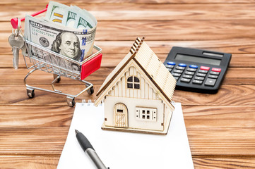 Wall Mural - Model of house on blank notepad with money in shopping cart  and calculator on the wooden background. Real estate agent's workplace.