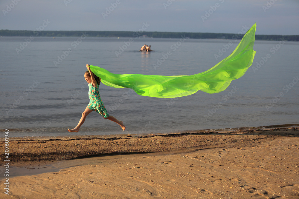 Młoda dziewczynka skacze przez wodę z długą zieloną chustą. - obrazy, fototapety, plakaty 