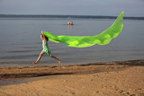 Fototapeta  - Młoda dziewczynka skacze przez wodę z długą zieloną chustą.
