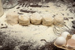 © Dmitrii - Shaped pieces of raw dough on wooden table with white wheat flour on black background. close-up
