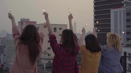 Wall Mural - Outdoor shot of young people at rooftop party. Happy group of asia girl friends enjoy and play sparkler at roof top party at evening sunset. Holiday celebration festive party. Teenage lifestyle party.