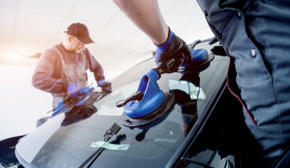 Automobile special workers replacing windscreen or windshield of a car in auto service station garage.