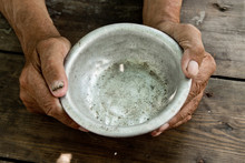 The Poor Old Man's Hands Hold An Empty Bowl Of Beg You For Help. The Concept Of Hunger Or Poverty. Selective Focus. Poverty In Retirement. Alms