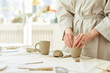 © pressmaster - Hands of female making mug from grey clay on table with supplies for creativity