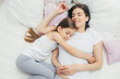 © VK Studio - Top view of cheerful mother sleeps on white bed near her daughter who embraces mum with great love, shows good attitude, have pleasant dreams and nice rest, wears pyjamas. People, sleeping concept
