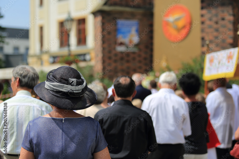 Kobieta w kapeluszu i zgromadzeni ludzie w czasie  nabożeństwa Bożego Ciała w Brzegu. - obrazy, fototapety, plakaty 