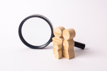 Wooden figures of people stand near the magnifying glass. The family is looking for something. The concept of housing search. Marketing, management. Human resources, social unit and statistics.