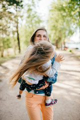 Happy smiling mother hugging her lovely little daughter outdoor. Lifestyle family. Adult cheerful female parent playing with her beautiful emotional child at nature in summer. Positive people faces.