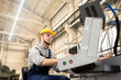 © Seventyfour - Portrait shot of bearded operator wearing protective helmet sitting in front of CNC machine and controlling manufacturing process, interior of production department on background