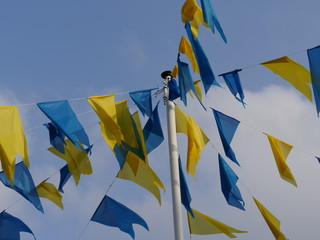 Details from  steel pole with a linen hung yellow and blue adornment  flags,  in front of a blue sky