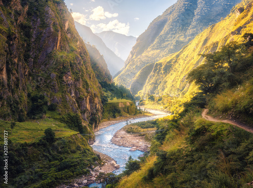 Cuadros en Lienzo Colorful landscape with high Himalayan mountains, beautiful curving river, green forest, blue sky with clouds and yellow sunlight at sunset in summer in Nepal