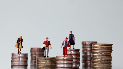 Wall Mural - Miniature people standing on piles of different heights of coins. The idea of a growing income gap between individuals.