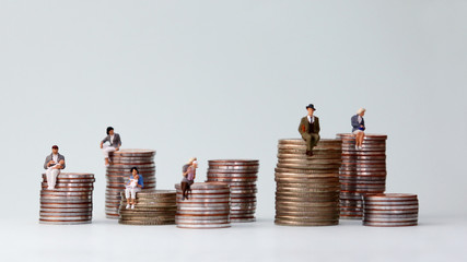 Wall Mural - Miniature people standing on piles of different heights of coins. The concept of the income gap between individuals that is not addressed.