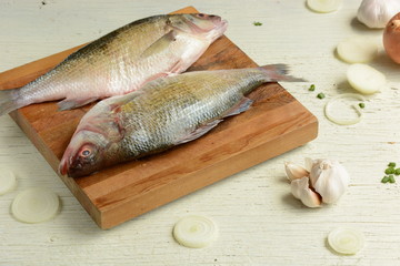 Fresh uncooked dorado or sea bream fish with lime, herbs,  vegetables and spices on rustic  wooden board over white backdrop, top view.   Healthy food or diet nutrition concept. 