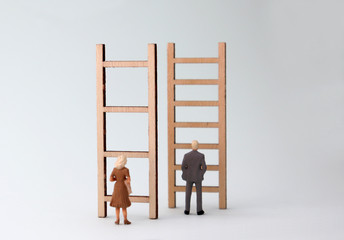 Wall Mural - Miniature men and women standing in front of different ladders. The concept of gender promotion discrimination in the workplace.