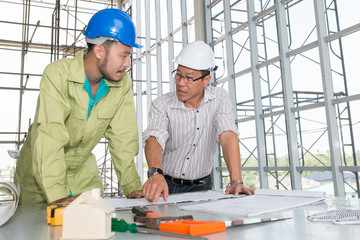 Asian male engineers wear helmet two. he looking at blueprints and talk construction plans analyzing brainstorming, teamwork, meeting concept.