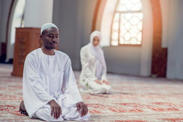 Black Muslim man and woman praying in mosque