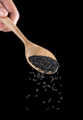 Canvas Print - Black sesame falling from wood spoon on black background