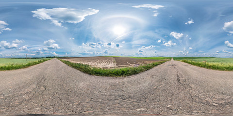 Wall Mural - full seamless spherical panorama 360 by 180 degrees angle view on the old asphalt road among fields in sunny summer day with halo in equirectangular projection, skybox VR virtual reality content