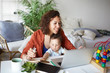 © shurkin_son - Attractive young dark skinned woman working at desk at home using laptop, holding baby on her lap. Portrait of smiling mother writing post on moms blog while her infant son playing with toy