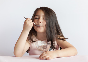 happy child girl eating ice cream in white and chocolate bowl on white background. enjoying deliciou