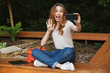 Sticker - Happy young girl taking selfie while sitting on a bench