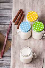 Wall Mural - Milk jars with colorful caps on a cutting board, cinnamon and drinking straw 