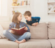 © Prostock-studio - Young girl reading book for her brother