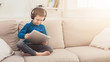 © Prostock-studio - Little boy using digital tablet on sofa at home